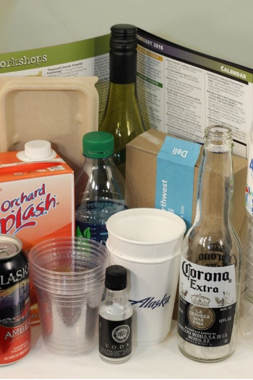 Can of amber ale, bottle of Corona, vodka, water bottle, paper and plastic cups, cardboard box, wine bottle.